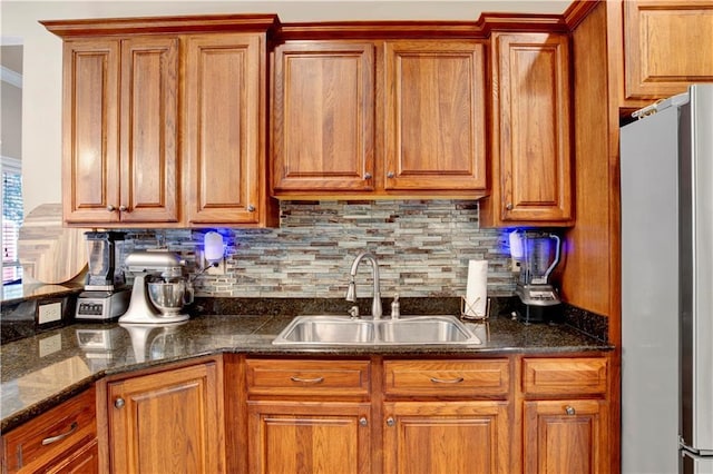 kitchen featuring sink, stainless steel fridge, backsplash, and dark stone counters