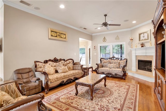 living room with a fireplace, ornamental molding, ceiling fan, and light wood-type flooring