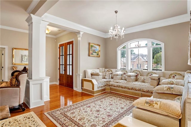 living room featuring crown molding, a notable chandelier, hardwood / wood-style flooring, and ornate columns