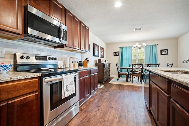 kitchen with dark hardwood / wood-style floors, an inviting chandelier, stainless steel appliances, and light stone countertops