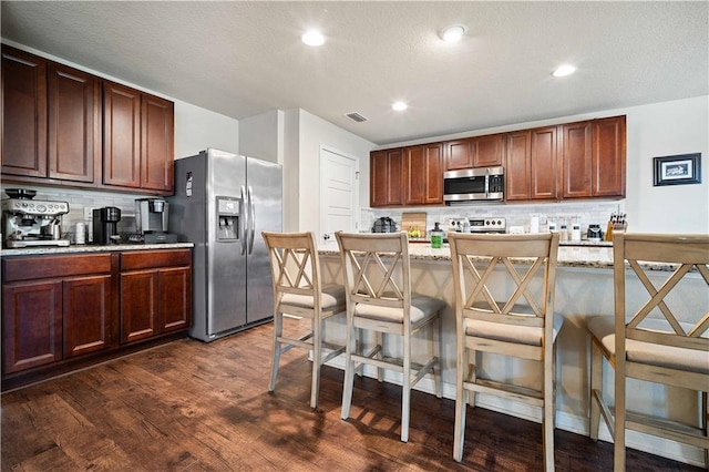 kitchen featuring light stone counters, stainless steel appliances, dark wood-type flooring, and a breakfast bar