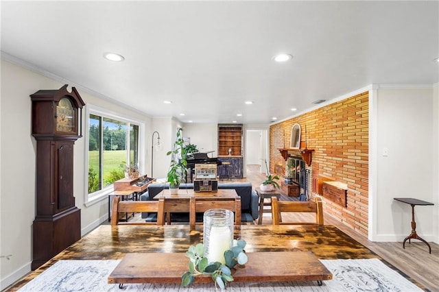 dining space featuring ornamental molding, a brick fireplace, wood-type flooring, and brick wall