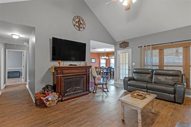 living room with high vaulted ceiling, a fireplace, wood finished floors, a ceiling fan, and attic access