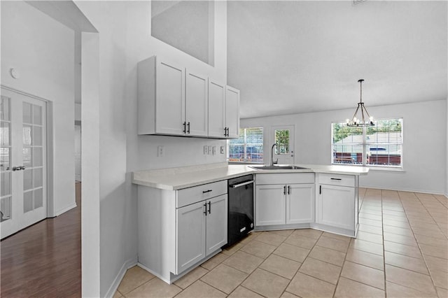 kitchen with white cabinets, black dishwasher, light tile patterned flooring, sink, and decorative light fixtures