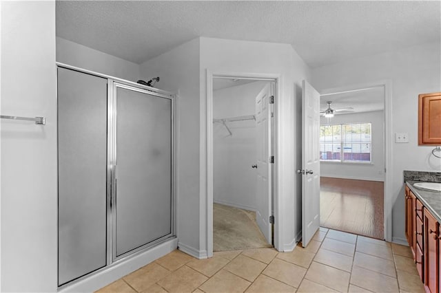 bathroom featuring ceiling fan, a textured ceiling, walk in shower, vanity, and tile patterned floors