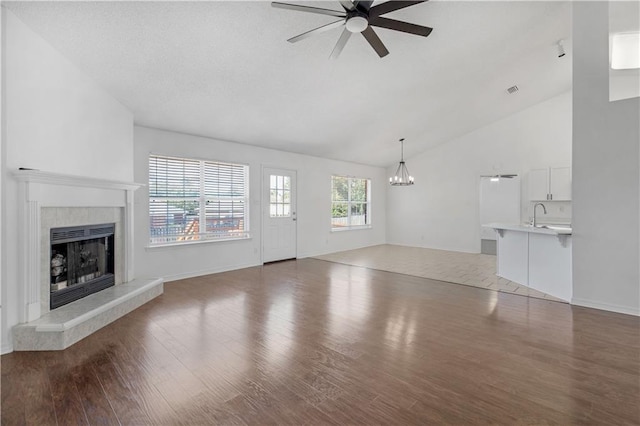 unfurnished living room with lofted ceiling, hardwood / wood-style floors, a tile fireplace, ceiling fan with notable chandelier, and sink