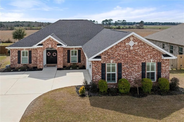 view of front facade with a shingled roof, brick siding, and driveway