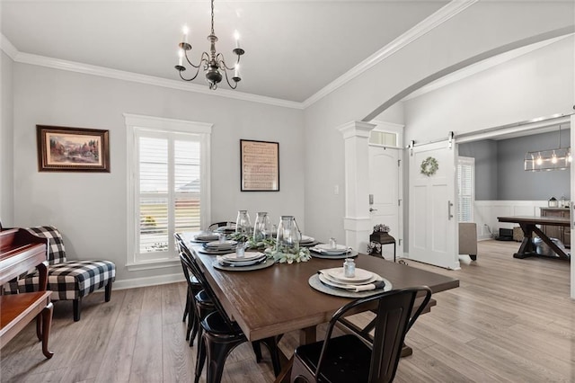 dining space featuring arched walkways, light wood-style flooring, an inviting chandelier, and a barn door