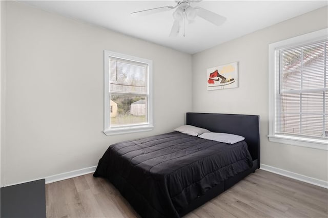 bedroom with multiple windows, wood finished floors, and baseboards