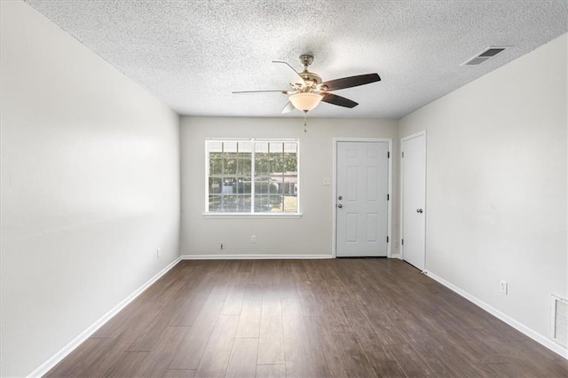 unfurnished room featuring a textured ceiling, dark wood-style flooring, baseboards, visible vents, and ceiling fan