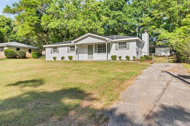 view of front of home featuring concrete driveway, a chimney, covered porch, a front yard, and brick siding