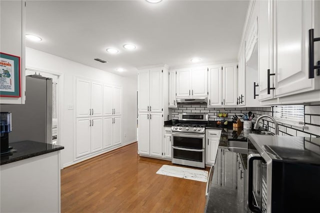 kitchen featuring backsplash, dark stone counters, stainless steel range oven, white cabinets, and hardwood / wood-style floors