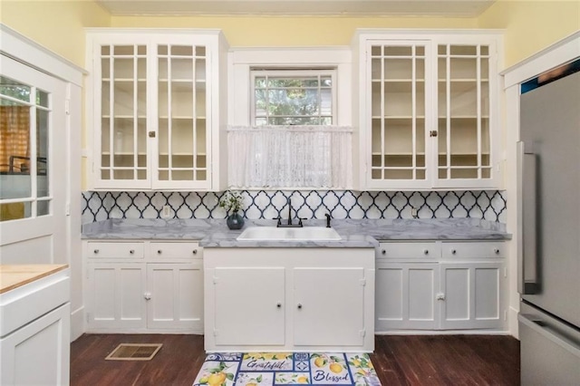 kitchen with tasteful backsplash, sink, white cabinets, and fridge