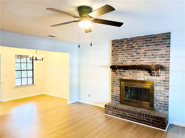 unfurnished living room with wood-type flooring, a fireplace, and ceiling fan with notable chandelier