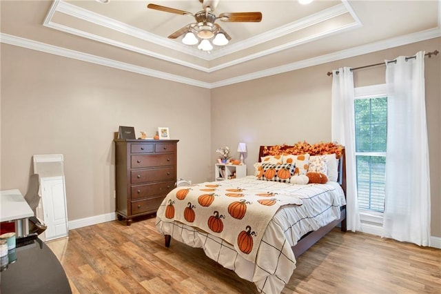 bedroom with ornamental molding, light wood-type flooring, ceiling fan, and a tray ceiling