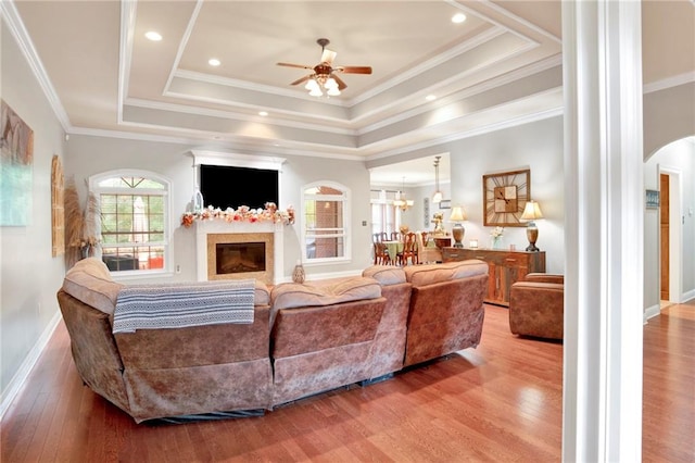 living room with hardwood / wood-style flooring, ceiling fan with notable chandelier, a raised ceiling, and crown molding