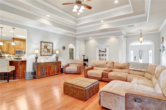 living room featuring a raised ceiling, ornate columns, light wood-type flooring, and crown molding