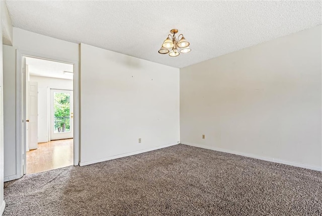 unfurnished room with a textured ceiling, an inviting chandelier, and carpet floors