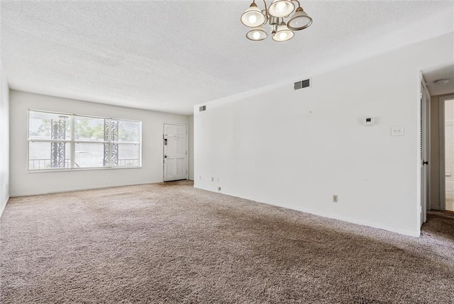 carpeted spare room featuring an inviting chandelier and a textured ceiling