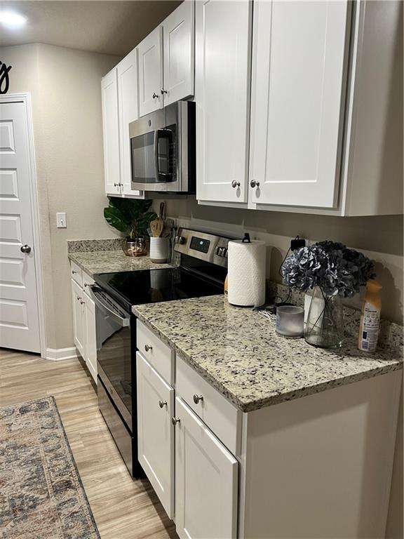 6157 Stream Bank Dr, Mobile, AL 36582 - kitchen featuring light wood-type flooring, white cabinets, light stone counters, stainless steel microwave, and electric range oven