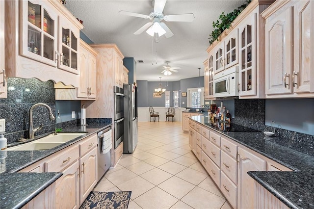 kitchen featuring light tile patterned floors, ceiling fan with notable chandelier, stainless steel appliances, a sink, and glass insert cabinets