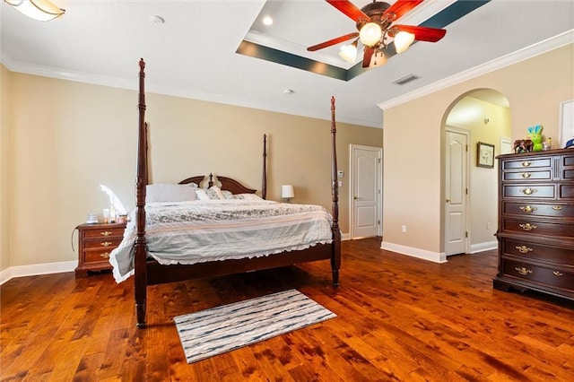 bedroom featuring ornamental molding, arched walkways, a raised ceiling, and wood finished floors