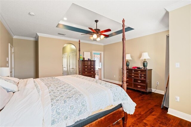 bedroom with wood finished floors, visible vents, baseboards, a raised ceiling, and crown molding