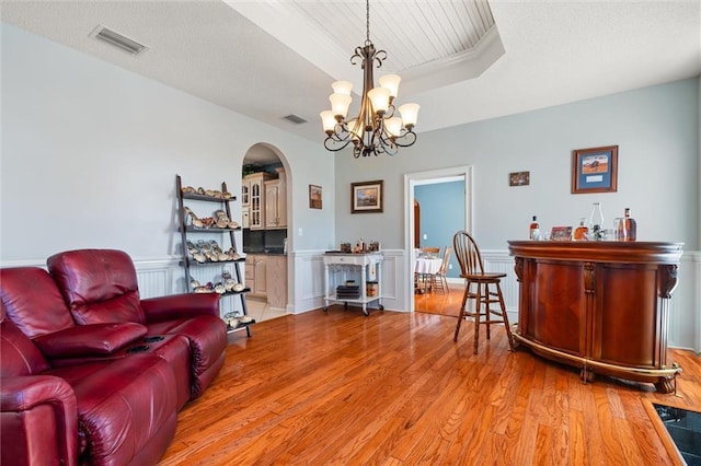 interior space with arched walkways, a raised ceiling, visible vents, and light wood finished floors