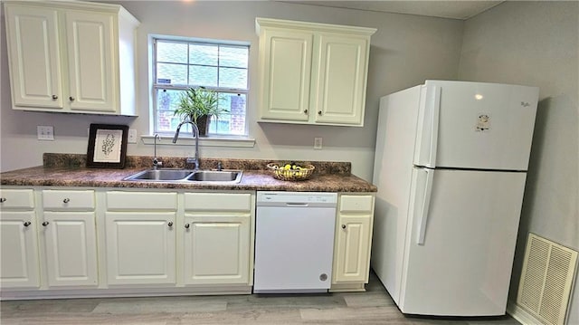 kitchen with visible vents, dark countertops, light wood-type flooring, a sink, and white appliances