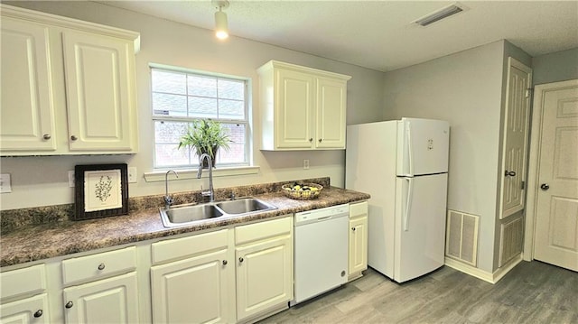 kitchen with visible vents, dark countertops, white appliances, a sink, and light wood-style flooring