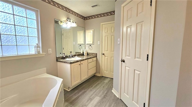 bathroom with wood finished floors, a bath, visible vents, and vanity