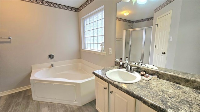 full bath featuring a bath, a stall shower, wood finished floors, vanity, and baseboards