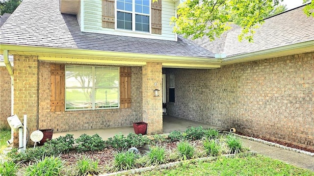 entrance to property with roof with shingles and brick siding