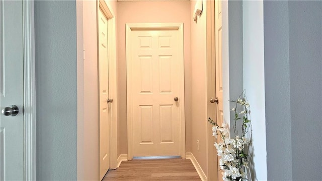 doorway featuring baseboards, a textured wall, and light wood-style flooring