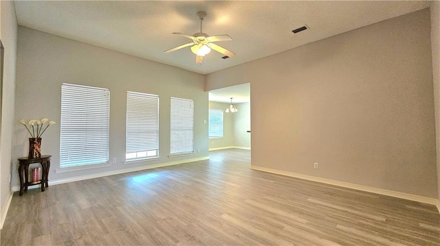 spare room featuring baseboards, visible vents, ceiling fan with notable chandelier, and light wood-type flooring