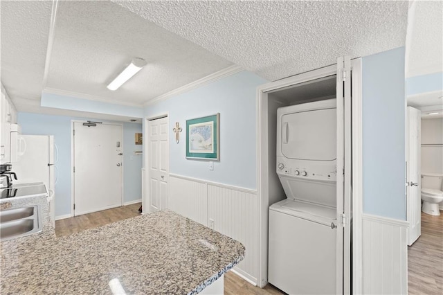 clothes washing area with a textured ceiling, crown molding, stacked washer / dryer, and sink