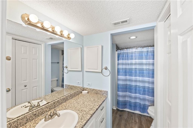 bathroom with a textured ceiling, hardwood / wood-style floors, vanity, and toilet