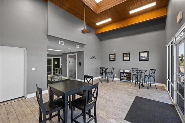 dining space featuring light wood-type flooring, wooden ceiling, and a towering ceiling