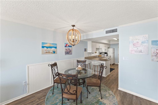 dining area featuring a textured ceiling, dark hardwood / wood-style flooring, crown molding, and a chandelier