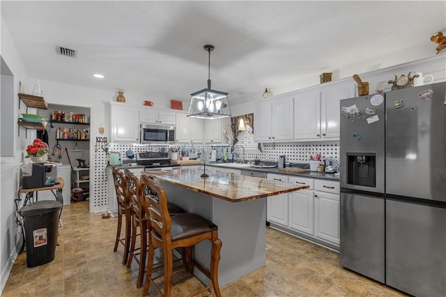 kitchen featuring white cabinetry, stainless steel appliances, a center island, tasteful backsplash, and decorative light fixtures