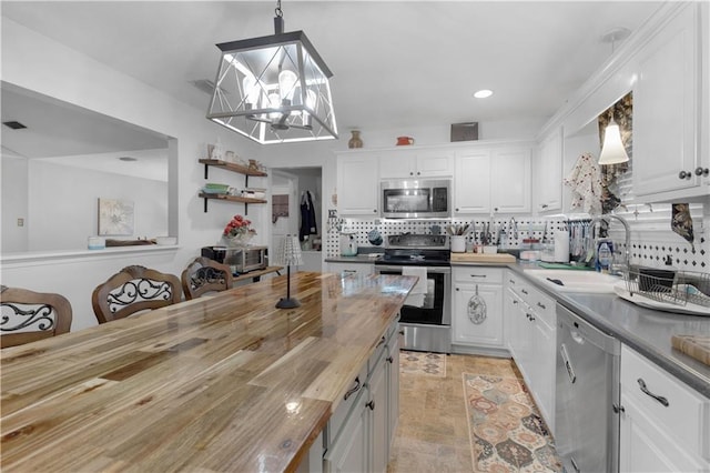 kitchen featuring stainless steel appliances, white cabinetry, wood counters, and decorative light fixtures