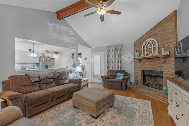 living room with ceiling fan, high vaulted ceiling, a fireplace, light hardwood / wood-style floors, and beamed ceiling