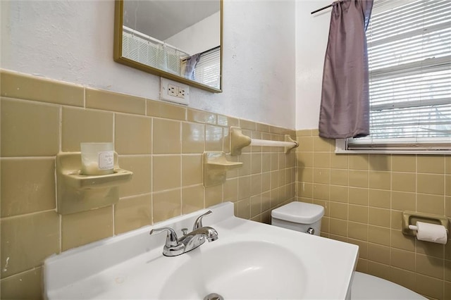 bathroom with a sink, tile walls, and toilet