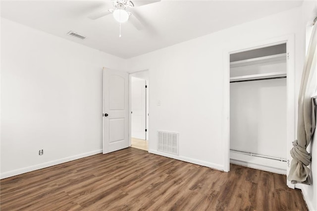 unfurnished bedroom with dark hardwood / wood-style flooring, a closet, ceiling fan, and baseboard heating