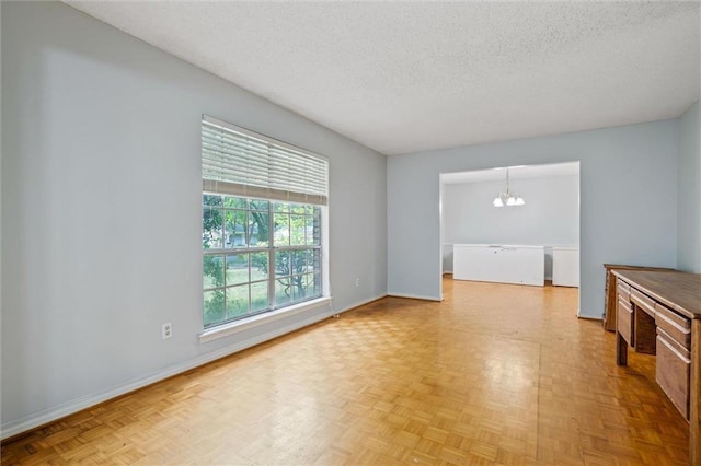 spare room featuring an inviting chandelier, baseboards, and a textured ceiling