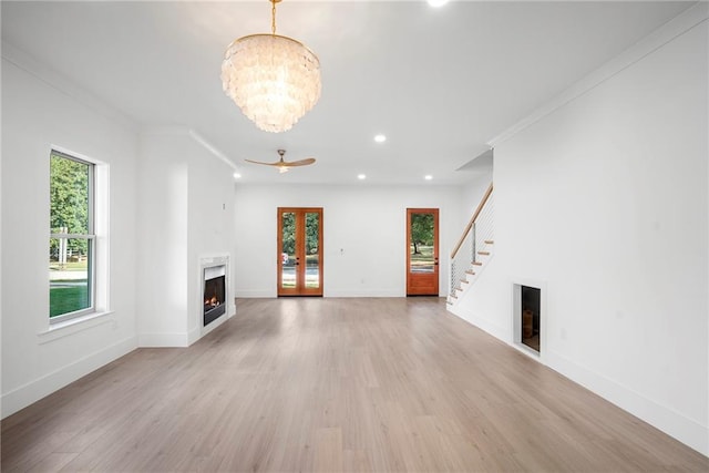 unfurnished living room featuring light hardwood / wood-style floors, ornamental molding, plenty of natural light, and ceiling fan with notable chandelier