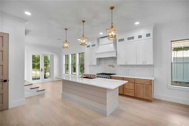 kitchen featuring white cabinetry, decorative light fixtures, premium range hood, and a center island with sink