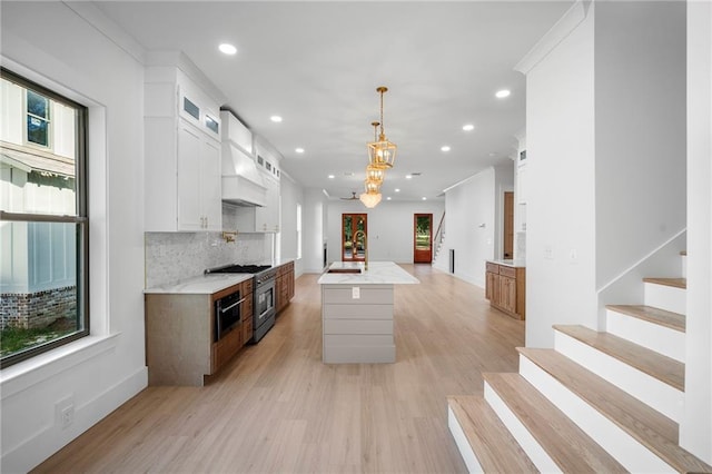 kitchen with white cabinetry, a center island with sink, light wood-type flooring, and pendant lighting