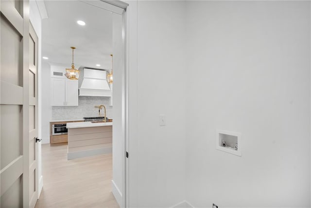 clothes washing area with sink, light hardwood / wood-style flooring, and washer hookup