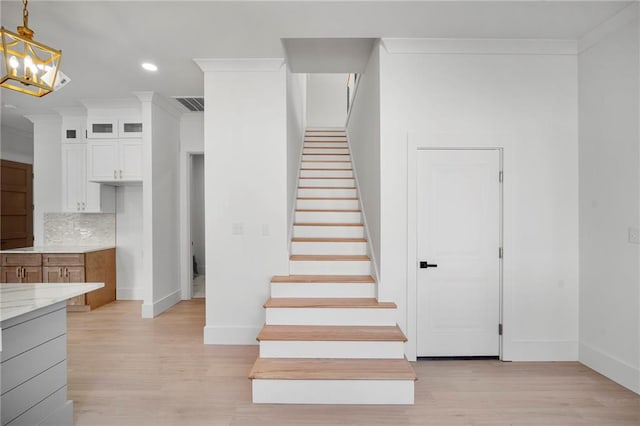 stairs with a notable chandelier, ornamental molding, and wood-type flooring